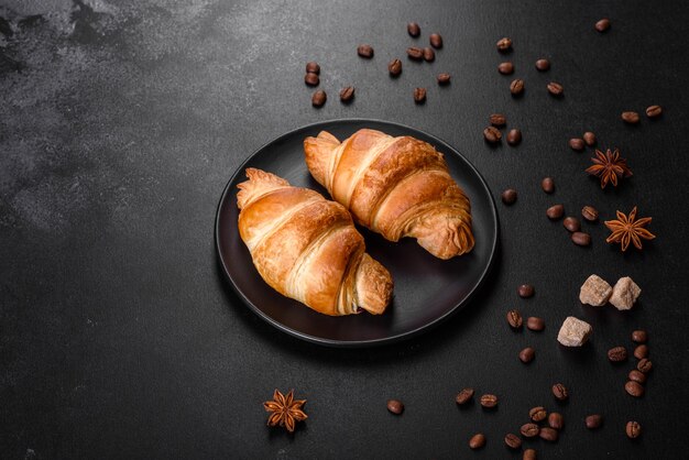 Crocante fresco e delicioso croissant francês com grãos de café na mesa preta