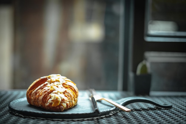 Croissant de almendras en la placa negra y cubiertos. Enfoque selectivo. de cerca