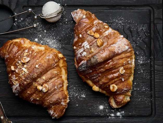 Croissant assado em uma placa de madeira e polvilhado com mesa preta de açúcar em pó pastéis apetitosos no café da manhã