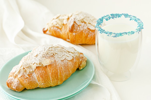 Croissant con azúcar en polvo y hojuelas de almendras, vaso de leche fresca