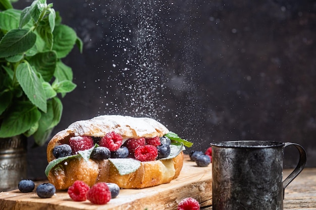 Croissant com framboesas, mirtilos e queijo creme numa tábua de madeira