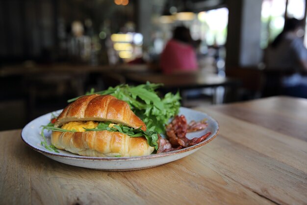 Croissant com ovo e bacon em fundo de madeira