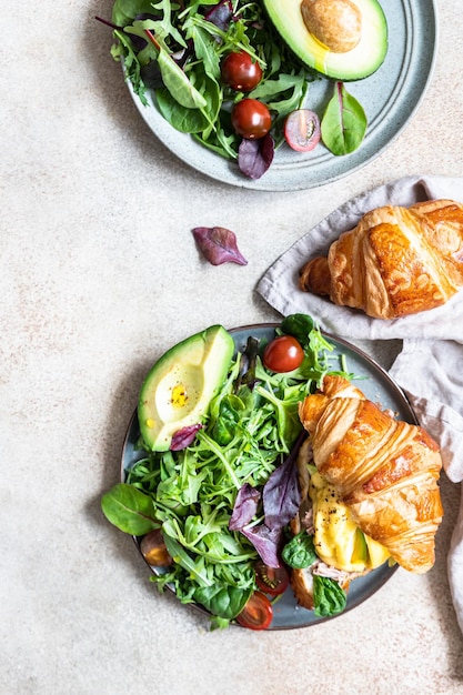 Croissant com ovo escalfado de atum, abacate e molho holandês com folhas de salada verde e tomate