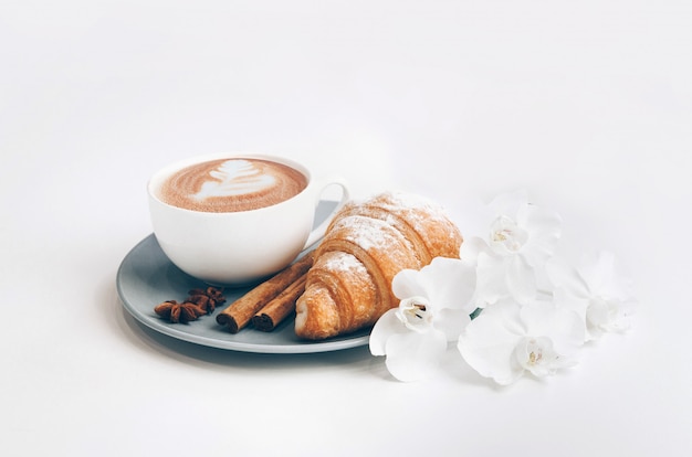 Croissant cozido fresco com xícara de café, paus de canela e flores