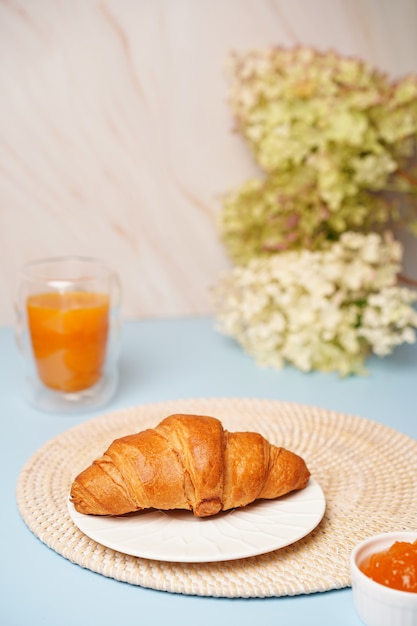 Croissant crocante em um fundo azul com geleia e suco de laranja, delicioso café da manhã. Foto de alta qualidade