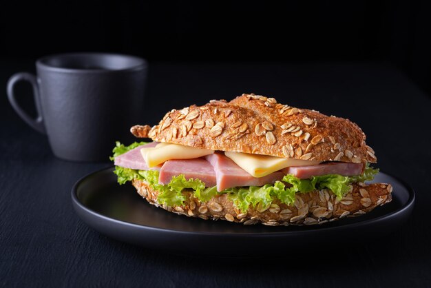 Croissant de sanduíche com presunto e queijo em uma mesa de madeira preta e café Conceito de comida de café da manhã