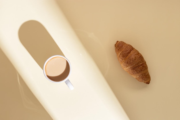 Croissant delicioso e xícara de café com leite em bege com luz solar café da manhã em um dia ensolarado de verão