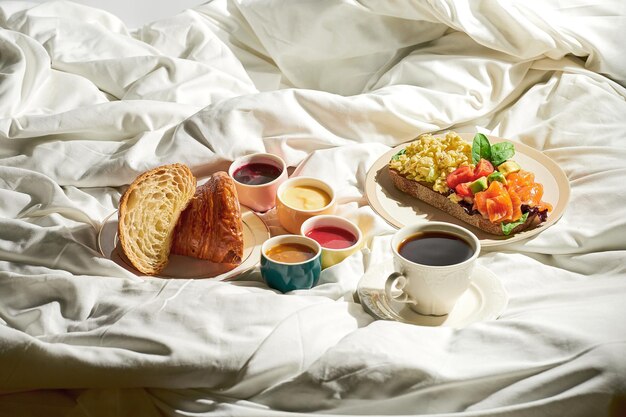 Croissant con diferentes toppings mermeladas y tostadas con huevos revueltos salmón en un plato sobre una sábana blanca Luz dura Un desayuno completo