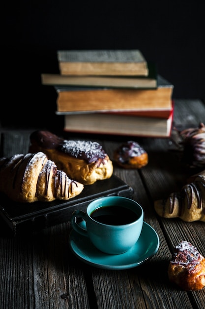 Croissant e xícara de café preto branco sobre tela marrom.