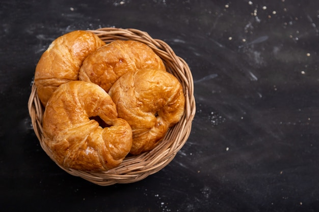 Foto croissant em uma cesta de vime colocada no chão preto