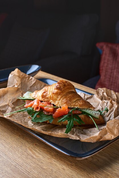 Croissant francês com fatias de salmão, abacate e espinafre na placa azul sobre uma mesa de madeira Foto para o menu