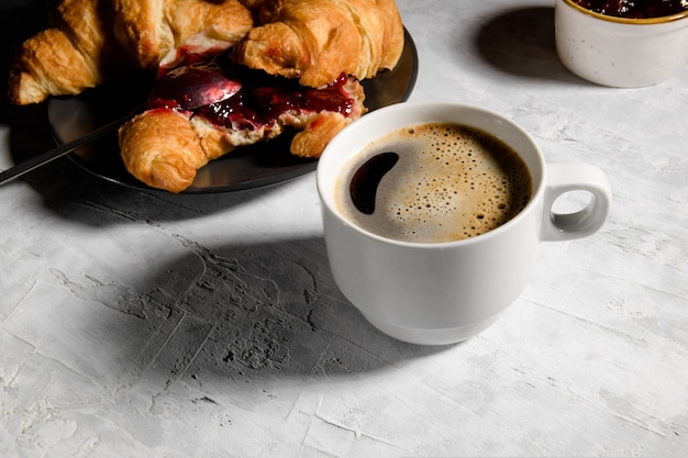 Croissant francés fresco con mermelada de cerezas en placa gris y tapa de café recién hecho