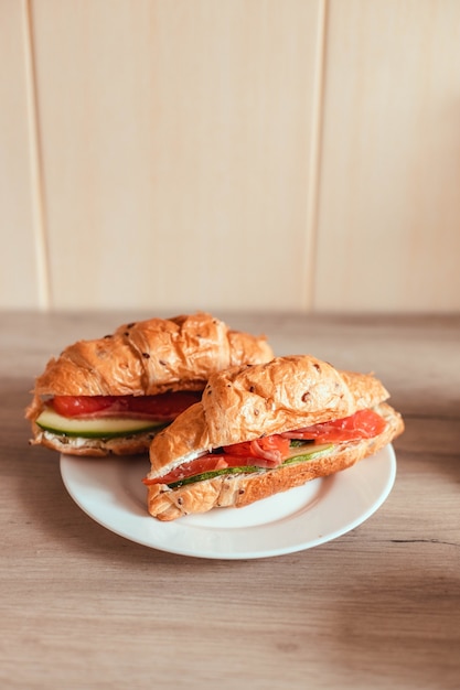 Croissant francés fresco con salmón y pepino en un plato sobre una mesa de madera.