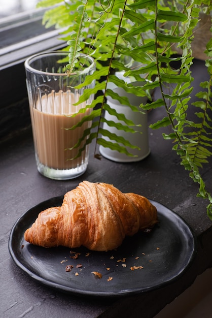 Foto croissant francés en una placa de luz junto a un vaso de café