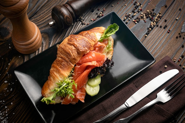 Croissant francés con salmón, ensalada, pepino y salsa en plato oscuro