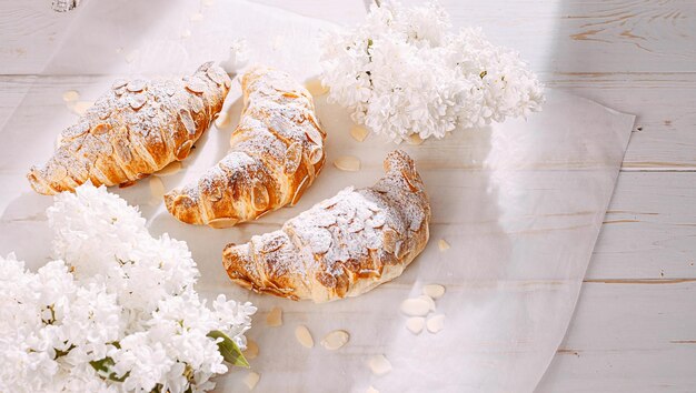 Croissant fresco com fatias de amêndoa em um fundo branco de madeira