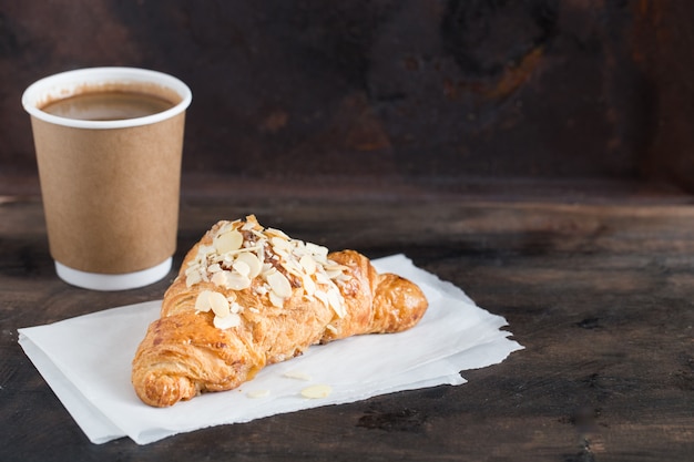 Croissant fresco e café em um copo de papel no escuro