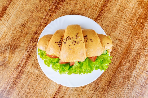 Croissant fresco con jamón y lechuga en una mesa de madera en un café. Croissant de verduras