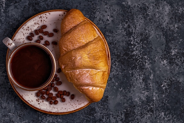 Croissant fresco sobre una superficie oscura con café