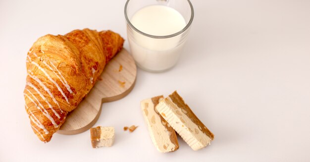 Croissant grande e caneca de vidro com suporte de leite em uma mesa branca