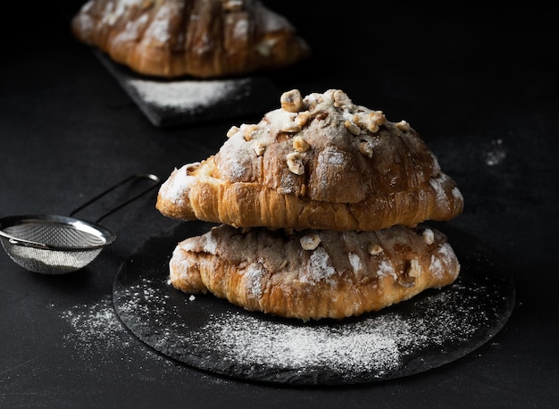 Croissant horneado sobre una tabla de madera y espolvoreado con mesa negra de azúcar en polvo Apetitosos pasteles para el desayuno