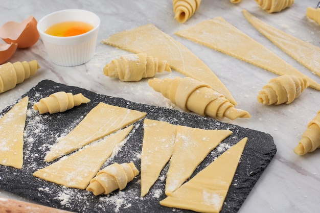 Croissant machen, Croissant aufgerollt auf weißem Marmortisch. Backvorbereitungsprozess in der Küche