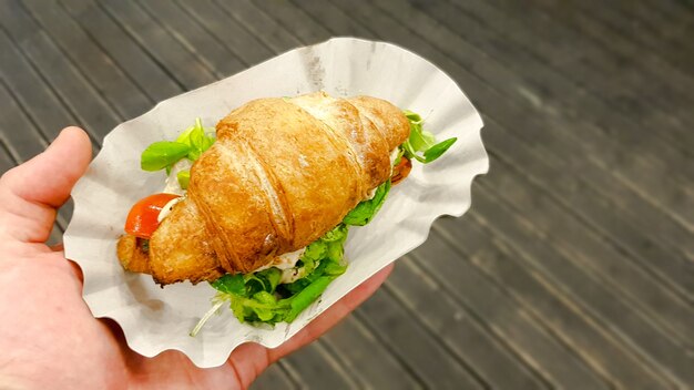 Croissant mit Avocado, Tomate und Kräutern im Freien. Vegetarisches Essen auf der Straße.