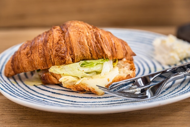Croissant mit gegrilltem Käse und Salat auf Teller, Holztisch im Café oder Café