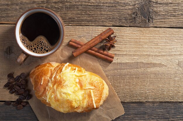 Croissant mit Käse und heißem Kaffee zum Frühstück auf altem Holzhintergrund, Draufsicht. Platz für Text