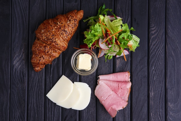 Croissant mit Schinken, Mozzarella, Salat und Butter. Ansicht von oben.
