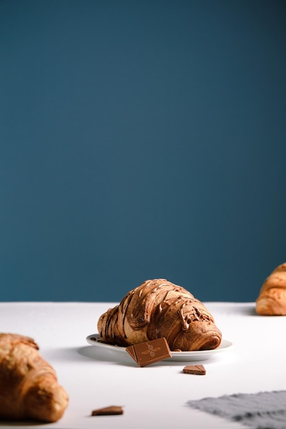 Croissant mit Schokolade Auf einem weißen Tisch und einem blauen Hintergrund ein Glas Cappuccino