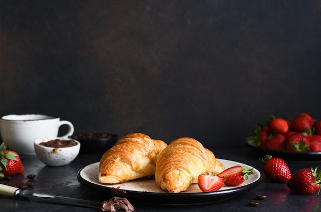 Croissant mit Schokoladenpaste und einer Tasse Kaffee, Erdbeeren auf dem Küchentisch. â€Traditioneller Snack oder FrÃ¼hstÃ¼ck.