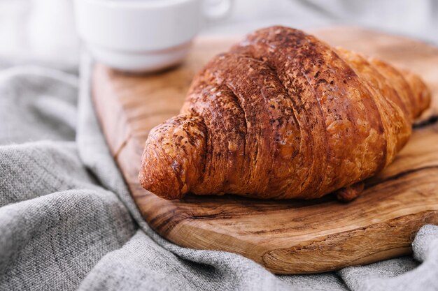 Croissant mit Schokoladenpulver auf einem Holzbrett