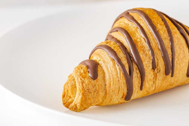 Croissant mit Schokoladenstreifen auf weißer Platte selektiver Fokus