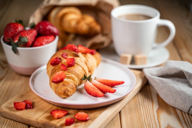 Croissant, morangos frescos e café em uma mesa de madeira