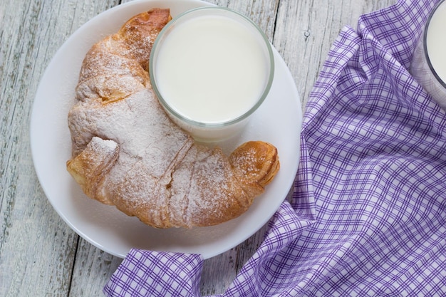 Croissant no prato com leite na velha mesa de madeira para fundo de café da manhã