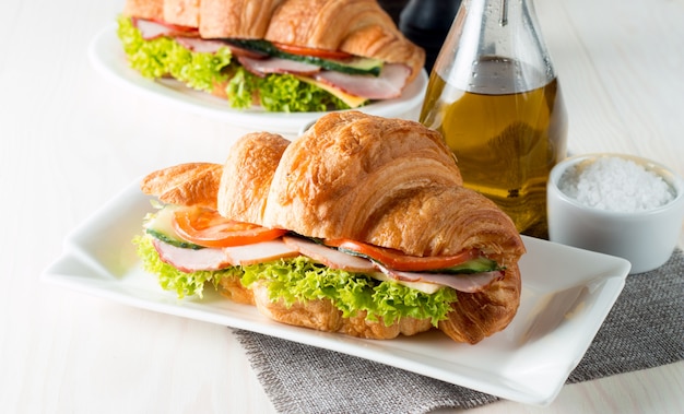 Croissant ou sanduíche fresco com salada, presunto no fundo de madeira.