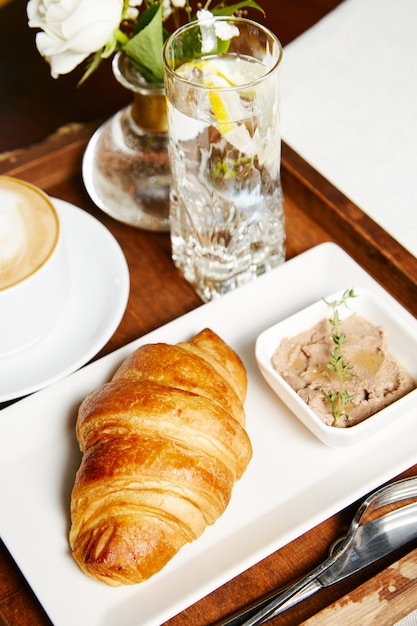 Croissant con paté y un vaso de agua con limón en una bandeja