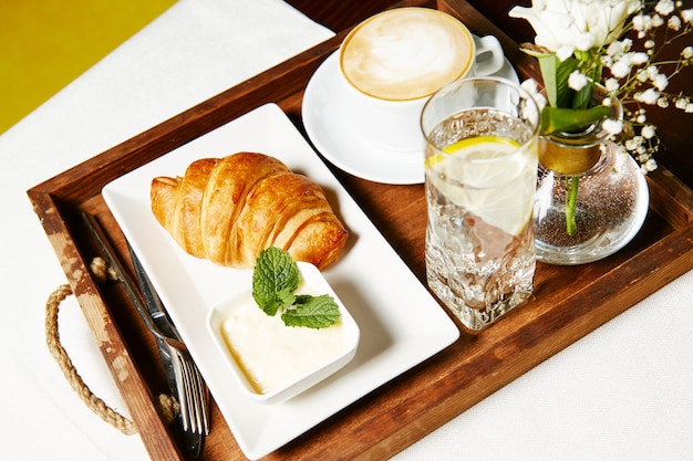 Croissant con paté y un vaso de agua con limón en una bandeja