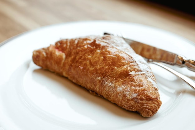 Un croissant en un plato blanco cubiertos en una ventana de madera.