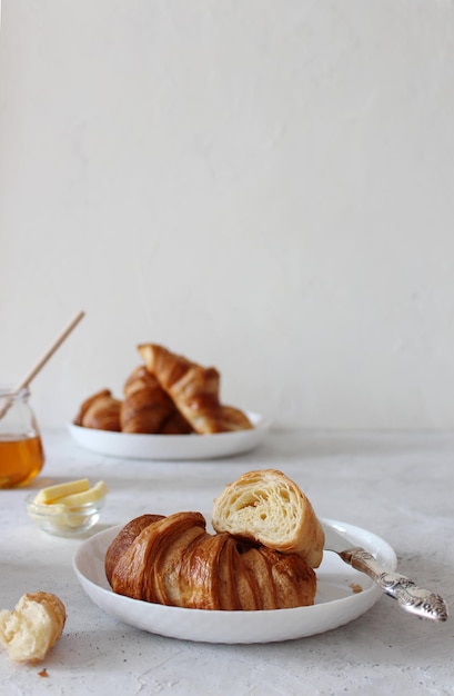 Croissant en el plato blanco con mantequilla y tarro de miel con cuchara de madera de miel en el fondo