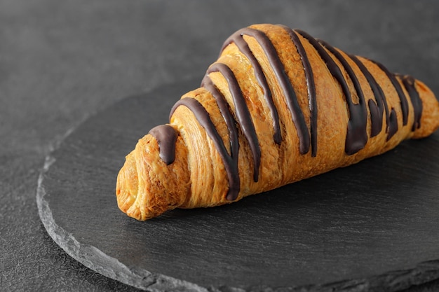 Croissant con rayas de chocolate en placa de piedra de pizarra redonda vista lateral de fondo oscuro enfoque selectivo