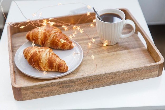 Croissant recém-assado em xícara branca de prato redondo cinza com café e guirlanda em uma bandeja sobre a mesa