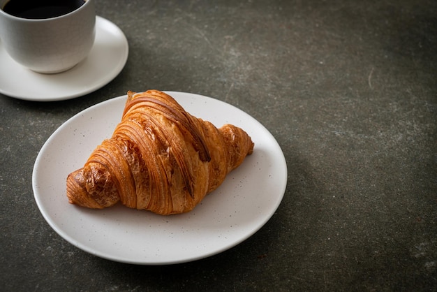 croissant recién hecho en un plato blanco con café negro