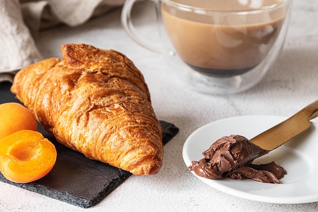 Croissant recién hecho, servido con albaricoques, chocolate para untar y café. Concepto de desayuno francés, gris b