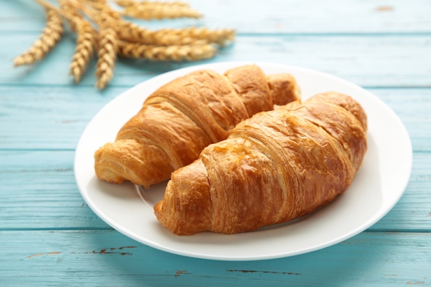 Croissant recién hecho con trigo sobre fondo azul.