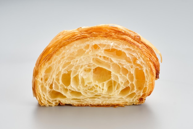 Foto croissant recién horneado sin relleno cortado sobre un fondo gris claro en una estructura porosa y aireada de un croissant sin relleno