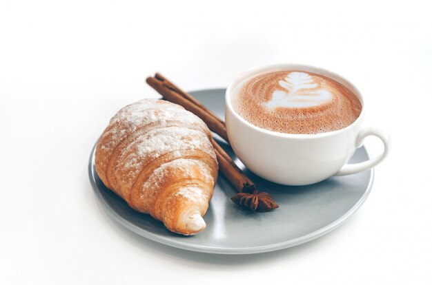 Croissant recién horneado con taza de café y café con leche, canela