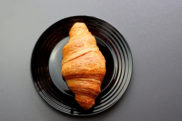 Croissant rubicundo en una placa negra sobre un gris.