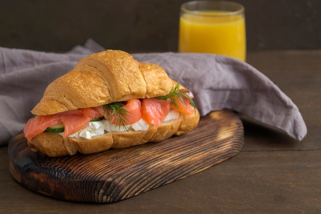 Foto croissant con salmón y queso crema sobre una plancha de madera.